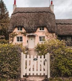 an old thatched house with a white picket fence