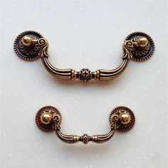 two gold colored handles and knobs on a white surface, one with an ornate design