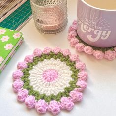 two crocheted coasters sitting on top of a table next to a mug