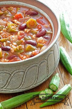 a bowl filled with beans and vegetables on top of a wooden table next to corn