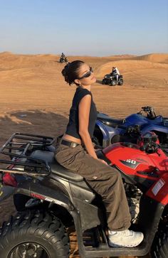 a woman is sitting on top of an atv in the middle of some sand dunes