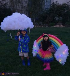 two children dressed up in costumes and holding umbrellas with lights on them, standing in the grass