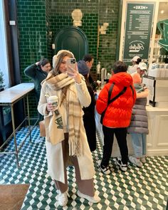 a woman taking a selfie in front of a green tiled wall with people standing around