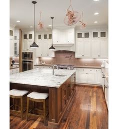 a large kitchen with white cabinets and wooden floors is pictured in this image, there are stools at the center of the island