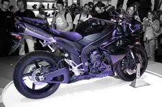 a black and purple motorcycle on display in front of a group of people with cameras