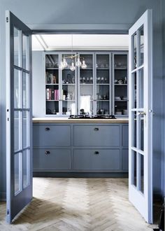 an open door leading to a kitchen with blue cabinets and wood flooring on the walls