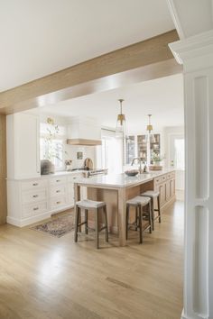 a large kitchen with white cabinets and wooden flooring is pictured in this image, there are stools at the center of the island