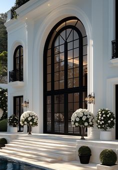 a large white house with black windows and flowers in the front yard, next to a swimming pool