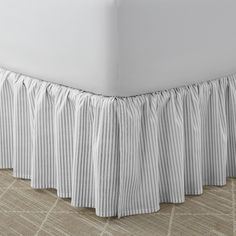 the bed skirt is made with pleated material and has a white stripe pattern on it