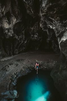 a person standing in the middle of a cave next to a body of blue water