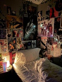 an unmade bed in a room with posters on the wall and candles lit up