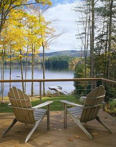 two adiron chairs on a deck overlooking a lake and trees in the fall season