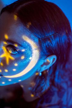 a woman's face with yellow stars painted on it and her eyes glowing blue