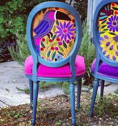 two chairs with painted designs on them sitting next to each other in front of some bushes