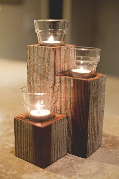 three candles are placed on wooden blocks with glass holders in the shape of trees and logs