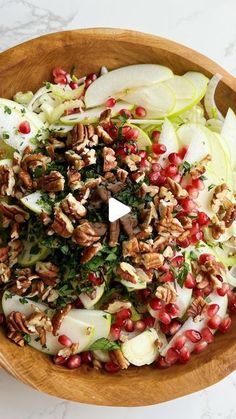 a wooden bowl filled with sliced apples, nuts and pomegranates on top of a marble counter