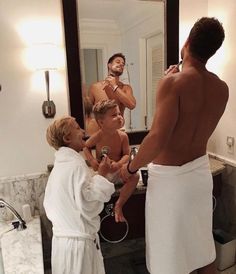 three men are in the bathroom and one is brushing his teeth while another man looks on