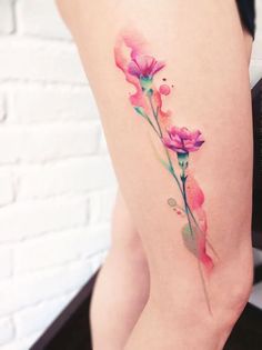 a woman's thigh with pink flowers on it and watercolor splashing paint