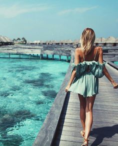 a woman walking along a pier next to the ocean