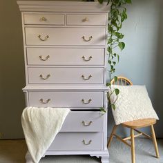 a white dresser sitting next to a chair with a plant growing on top of it