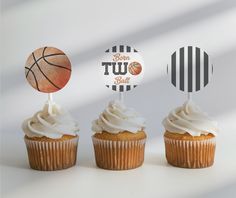 three cupcakes with white frosting and two basketball toppers on each one