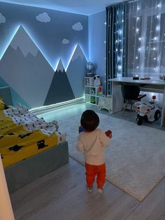 a small child standing in a room with mountains on the wall and lights behind him