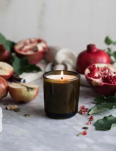 a candle that is sitting in front of some apples and pomegranates