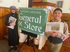 two people standing next to a sign that reads general store and the man is holding newspaper