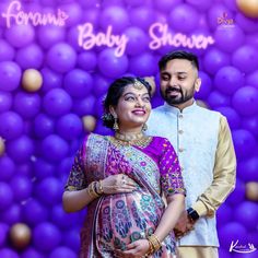 a man and woman standing next to each other in front of a backdrop with balloons