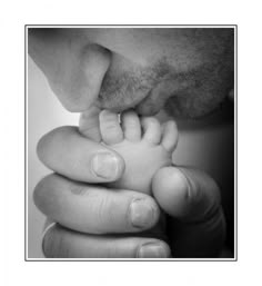 a black and white photo of a man holding a baby's hand