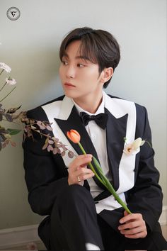 a young man in a tuxedo holding a flower and looking at the camera