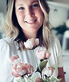 a woman holding a vase with pink flowers in it's hands and smiling at the camera