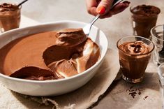 a person is spooning chocolate into a bowl with ice cream in it and two glasses on the side