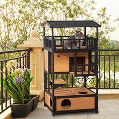 a cat sitting on top of a wooden house next to a potted plant and fence