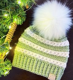 a green and white knitted hat next to a pine tree with lights on it