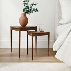 two wooden tables sitting on top of a hard wood floor next to a white bed