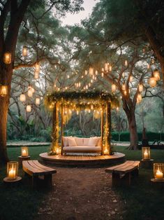 an outdoor seating area with lanterns hanging from the trees and lights on the ground above it