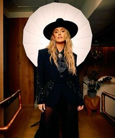 a woman in a black suit and hat posing for a photo with an umbrella over her head