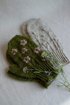 two knitted mittens with flowers on them sitting on a white cloth covered table