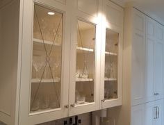 a kitchen with white cabinets and wine glasses on the glass front cabinet, along with an ice bucket