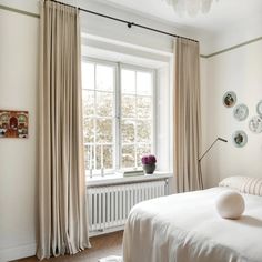 a white bed sitting next to a window in a bedroom under a chandelier