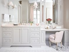 a large bathroom with white cabinets and marble counter tops, along with a pink chair