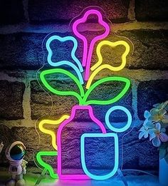 a vase with flowers is lit up by neon lights on a table next to a brick wall