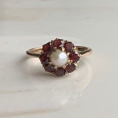 A vintage 9 carat gold Garnet and Pearl cluster ring.  CONDITION: Wear consistent with age and use. Please see photos for more detail. Stones all in good condition. HALLMARKED 9 CARAT GOLD, ASSAYED IN LONDON 1957 SETTING DIAMETER: 10mm  GARNET SIZE: 3mm (0.10 carats) PEARL SIZE: 4mm (0.33 carats) BAND WIDTH NARROWEST: 1.5mm RING SIZE: UK: J | US: 4 3/4 WEIGHT: 2.3 grams (SZ) 50s Wedding Ring, Garnet And Pearl Ring, Vintage Rings Antiques, Elizabeth Taylor Ring, Vintage Pearl Rings, Garnet And Pearl, Pearl Cluster Ring, Pearl Rings Vintage, Wire Wrap Jewelry Designs