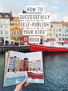 a person is holding an open book in front of the water with boats on it