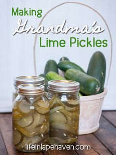 two jars filled with pickles sitting on top of a wooden table next to cucumbers