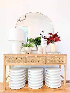 a wooden table topped with white plates and vases next to a large round mirror