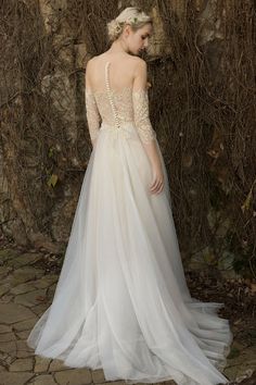 a woman in a wedding dress standing next to a stone wall with vines on it