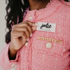 a close up of a person wearing a name tag on her jacket and holding onto some gold bracelets