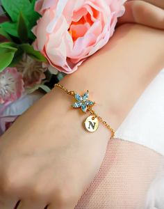 a close up of a person's arm with a flower and initial charm on it